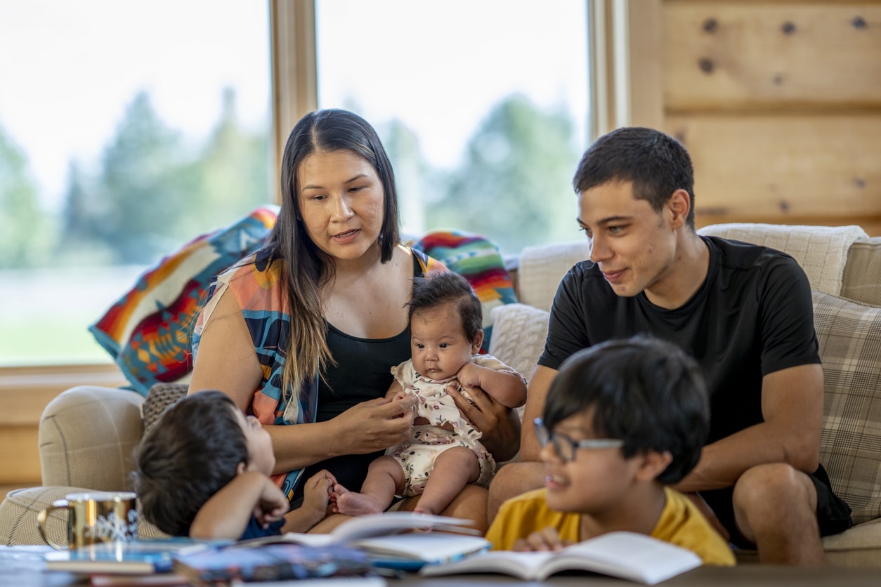 An Indigenous mother sits with her children of various ages, talking to them about the Sooke Family Resource Society.